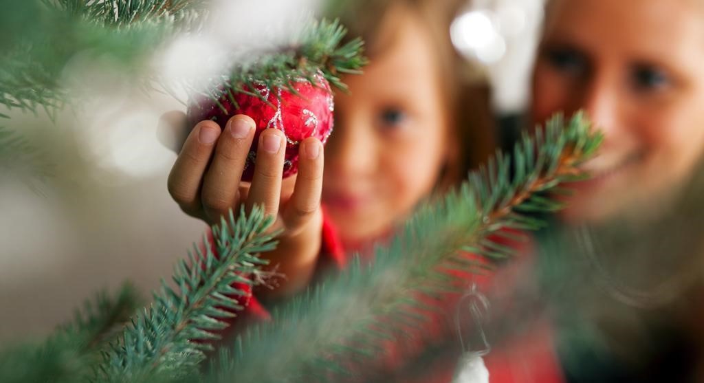 ett barn håller i en julkula med gran omkring sig.
